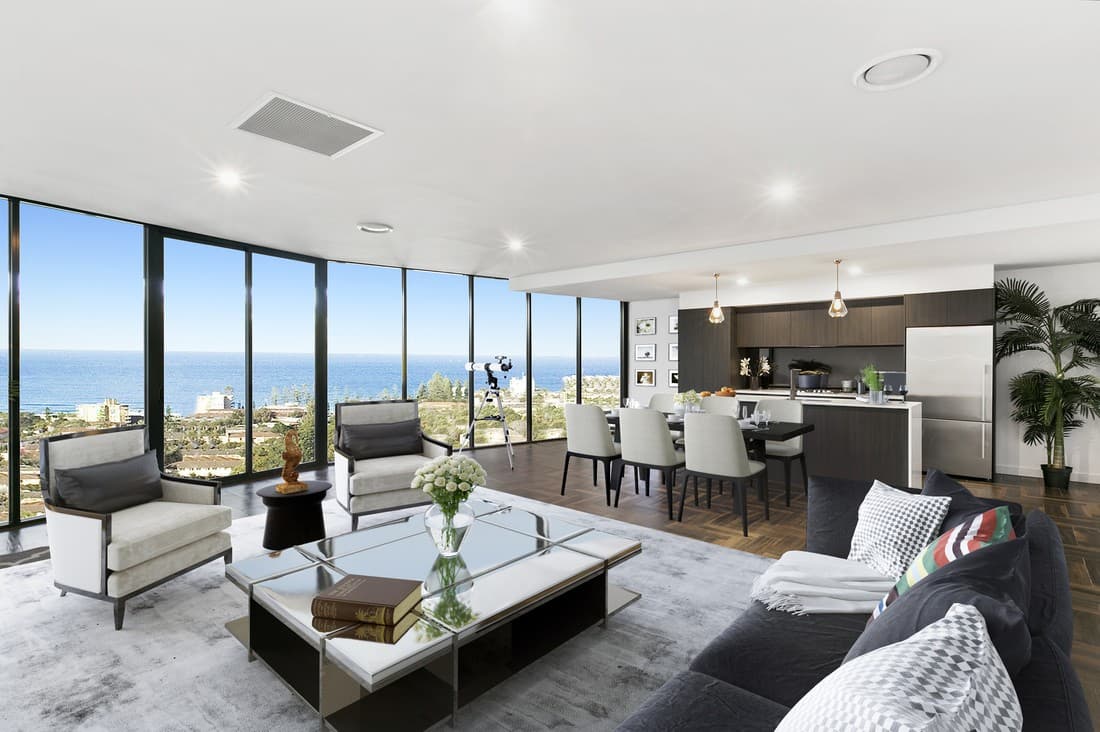 The same living room virtually staged with a sectional sofa, coffee table, armchairs and a large area rug, with the ocean view unchanged.